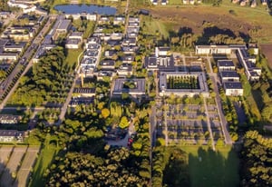 Aerial view of Roskilde University campus, showcasing buildings, green spaces, and pathways from a bird's-eye perspective.