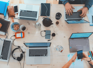 Image of computers and clutter on table with people working