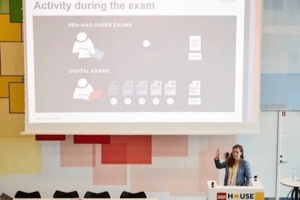 The image shows a presentation scenario with a person standing behind a podium with a LEGO HOUSE sign, gesturing towards a screen that displays icons and text related to 'Activity during the exam'.